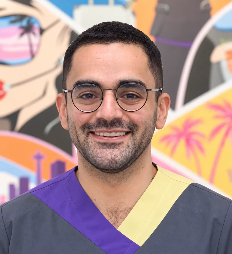 Dr Hossam Hafez smiling in Smileworks scrubs in front of the colourful practice mural.